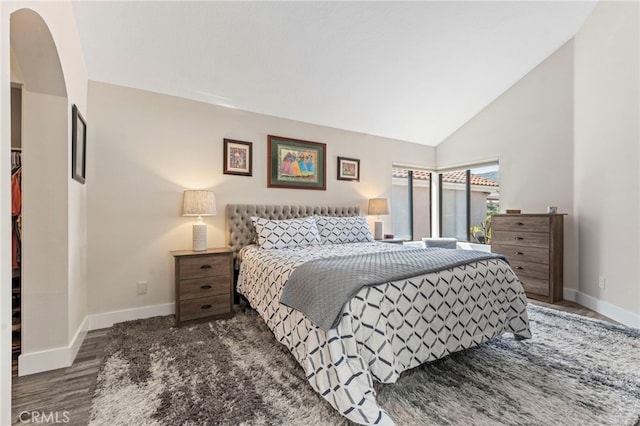 bedroom with baseboards, arched walkways, wood finished floors, and high vaulted ceiling