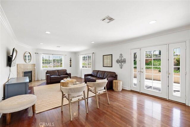 living area featuring crown molding, a tiled fireplace, wood finished floors, and visible vents