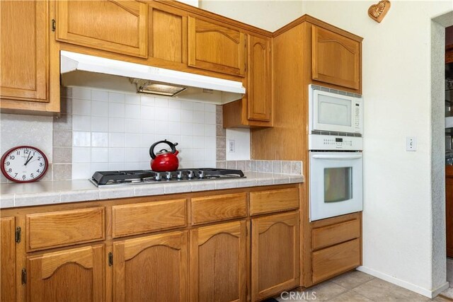 kitchen featuring backsplash, under cabinet range hood, white appliances, and tile countertops