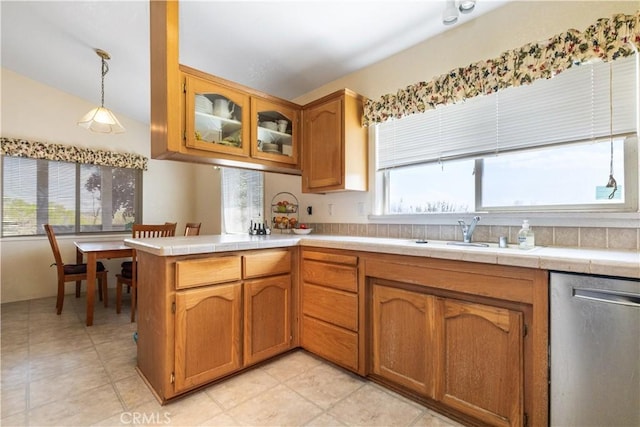 kitchen with glass insert cabinets, brown cabinetry, a peninsula, dishwasher, and decorative light fixtures