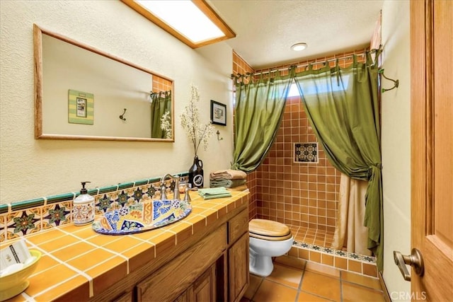 bathroom with vanity, toilet, tile patterned flooring, and tiled shower