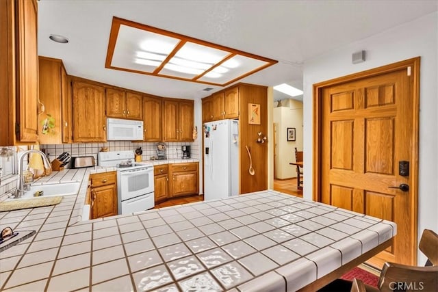 kitchen featuring a sink, tile countertops, decorative backsplash, white appliances, and a peninsula