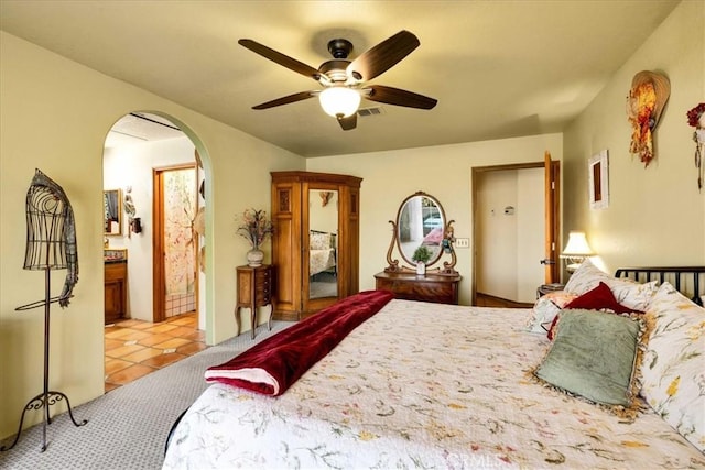 bedroom featuring arched walkways, connected bathroom, a ceiling fan, and light tile patterned floors