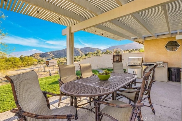view of patio featuring a grill, a mountain view, fence, an outdoor kitchen, and outdoor dining area