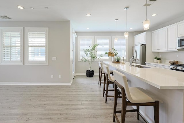 kitchen featuring a kitchen breakfast bar, light wood-style flooring, visible vents, a sink, and stainless steel appliances