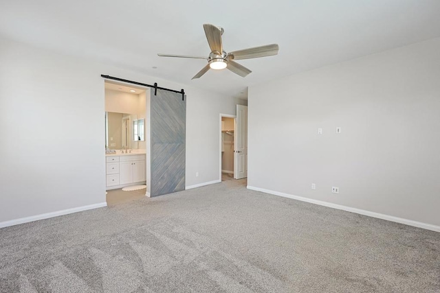 unfurnished bedroom with connected bathroom, a barn door, light carpet, a walk in closet, and baseboards