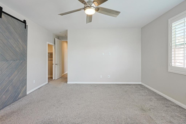 carpeted empty room with a healthy amount of sunlight, ceiling fan, baseboards, and a barn door
