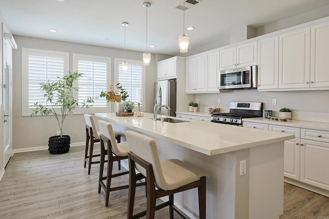 kitchen featuring light wood-style flooring, visible vents, appliances with stainless steel finishes, a sink, and a center island with sink