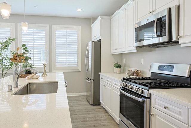 kitchen featuring light wood-style floors, appliances with stainless steel finishes, a sink, and white cabinetry