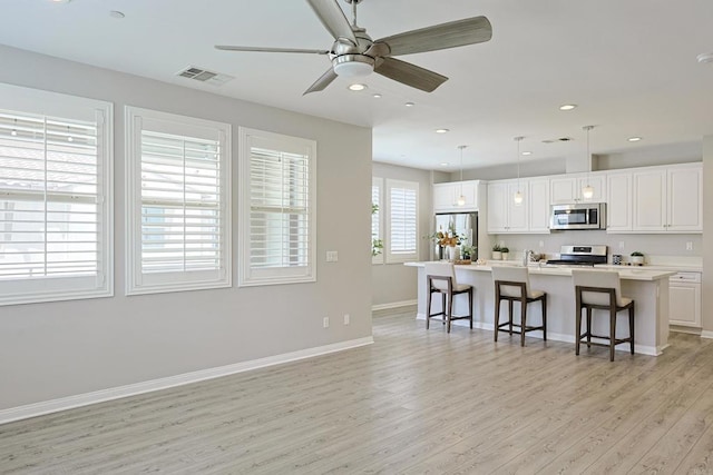 kitchen featuring a kitchen breakfast bar, light wood-type flooring, white cabinetry, appliances with stainless steel finishes, and baseboards