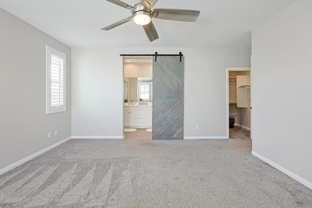unfurnished bedroom featuring baseboards, a barn door, carpet, a walk in closet, and ensuite bath