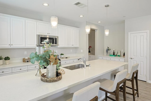 kitchen with stainless steel microwave, a breakfast bar, white cabinets, visible vents, and a sink