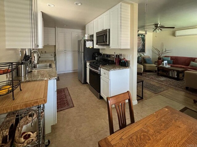 kitchen featuring a ceiling fan, white cabinets, a wall unit AC, stainless steel appliances, and a sink