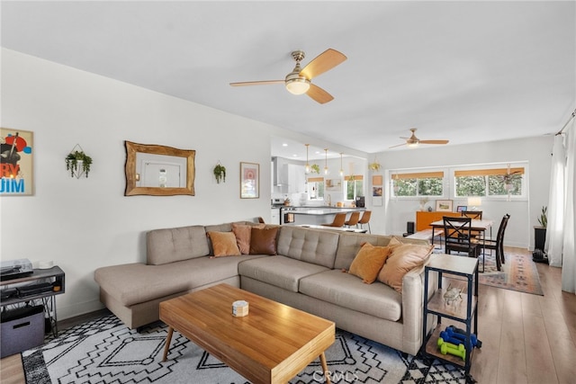 living room with light wood-style floors, baseboards, and a ceiling fan