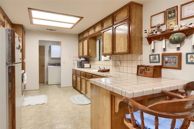 44410 Quail Ct, Coarsegold, CA 93614 - kitchen featuring tasteful backsplash, freestanding refrigerator, washer / dryer, brown cabinetry, and a sink