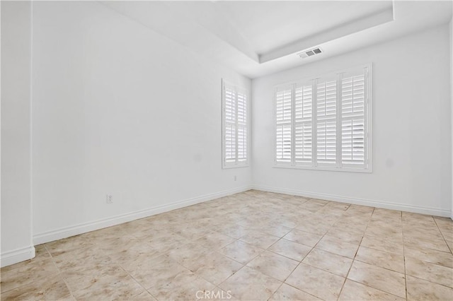 tiled empty room featuring a raised ceiling, baseboards, and visible vents