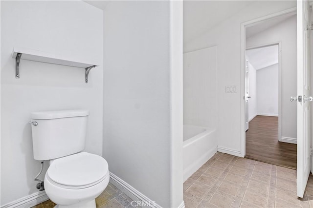 bathroom featuring baseboards, a tub, and toilet
