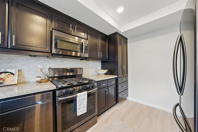 kitchen with decorative backsplash, light wood-type flooring, light stone counters, baseboards, and appliances with stainless steel finishes