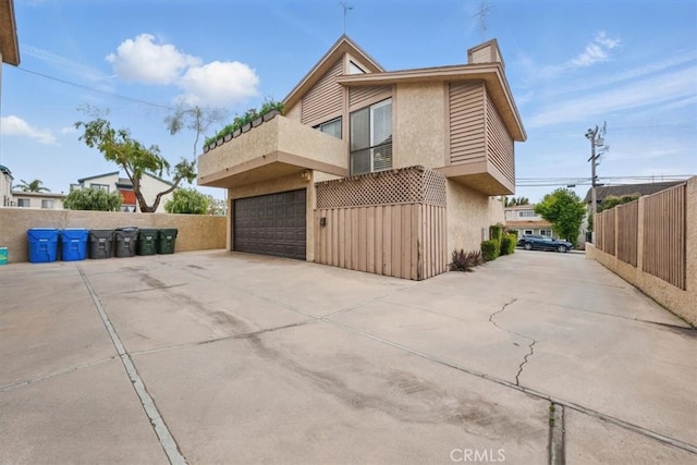 view of side of home with a garage, a balcony, a chimney, stucco siding, and fence
