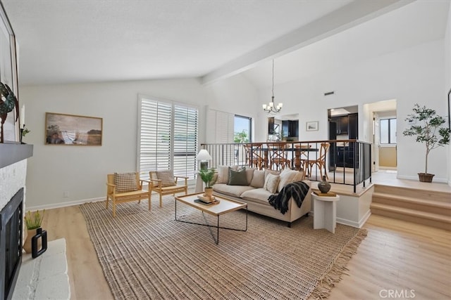 living room with vaulted ceiling with beams, an inviting chandelier, light wood finished floors, a fireplace with raised hearth, and baseboards