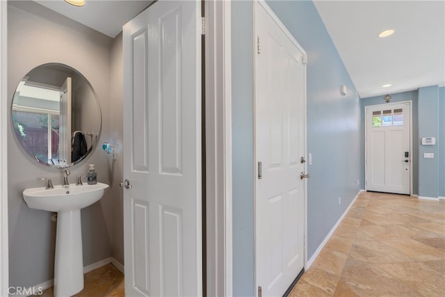 corridor featuring recessed lighting, stone finish flooring, baseboards, and a sink