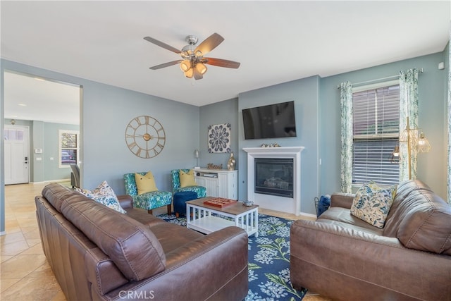 living area with baseboards, a glass covered fireplace, ceiling fan, and light tile patterned flooring