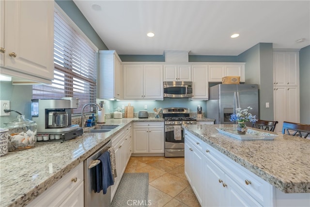 kitchen with white cabinets, a sink, light stone countertops, a center island, and appliances with stainless steel finishes