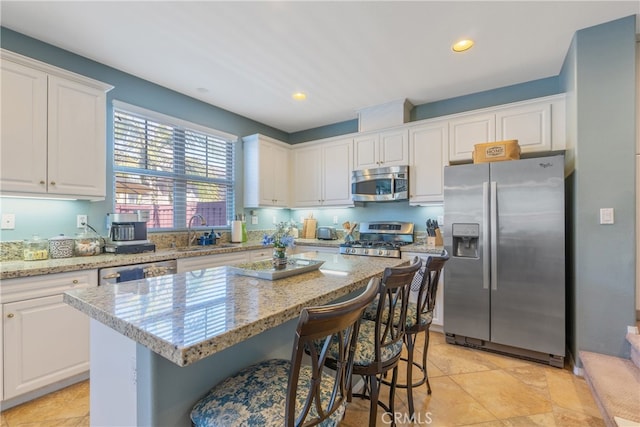 kitchen featuring white cabinets, a center island, a kitchen breakfast bar, a sink, and appliances with stainless steel finishes