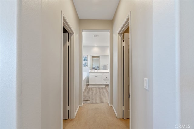 corridor featuring light carpet, visible vents, and baseboards