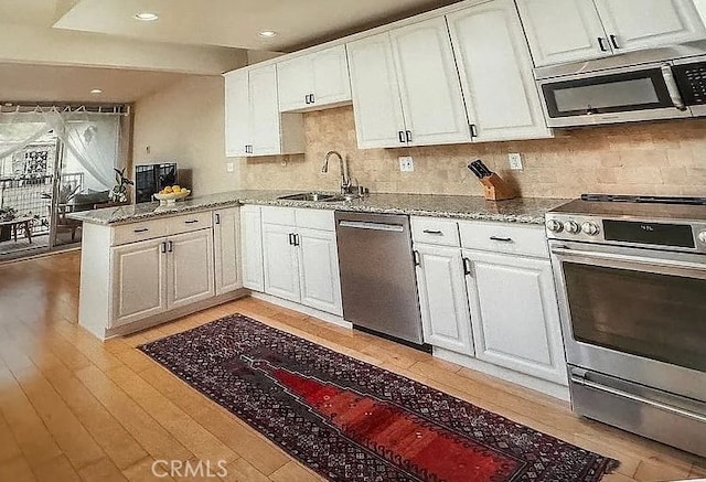 kitchen featuring a sink, appliances with stainless steel finishes, light stone counters, and white cabinetry