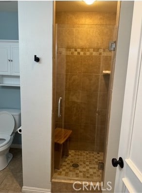 full bathroom with a shower stall, tile patterned flooring, baseboards, and toilet