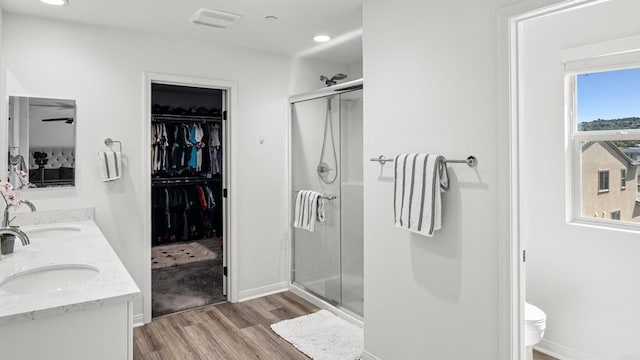 bathroom with a spacious closet, wood finished floors, a shower stall, and a sink