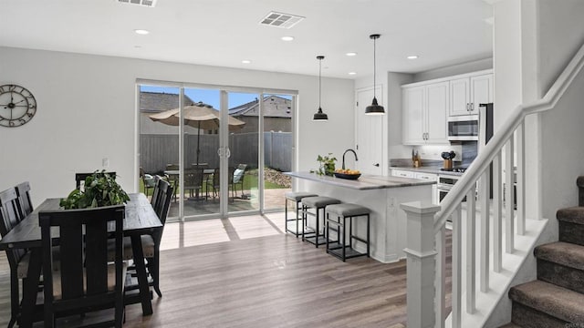 kitchen with stainless steel microwave, light wood-style floors, a kitchen breakfast bar, visible vents, and white cabinets