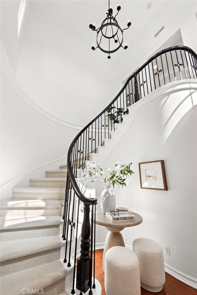 stairway featuring a high ceiling, an inviting chandelier, visible vents, baseboards, and wood finished floors