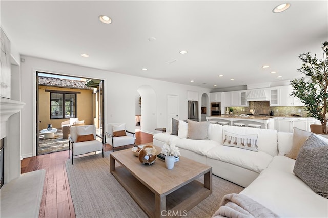 living area with a fireplace with raised hearth, baseboards, wood-type flooring, arched walkways, and recessed lighting