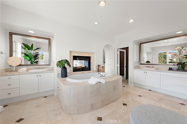 bathroom with recessed lighting, two vanities, a bath, and a sink