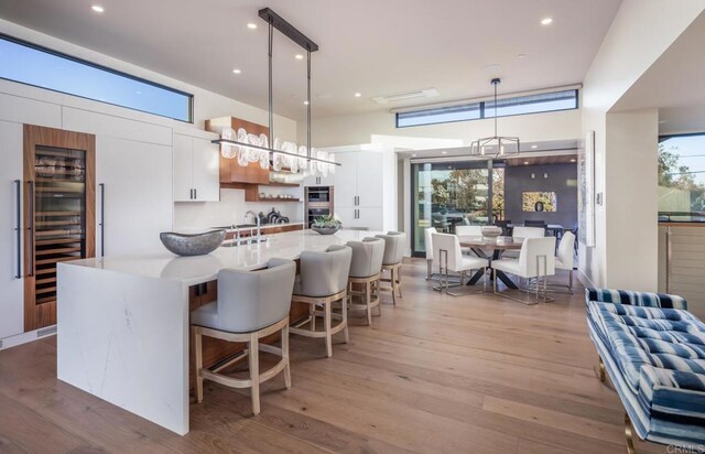 5170 Carlsbad Blvd, Carlsbad, CA 92008 - kitchen with beverage cooler, white cabinetry, light wood-style floors, decorative light fixtures, and a breakfast bar