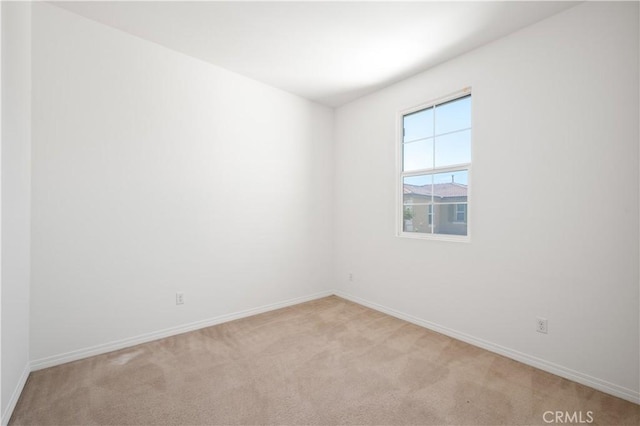 spare room featuring light carpet and baseboards
