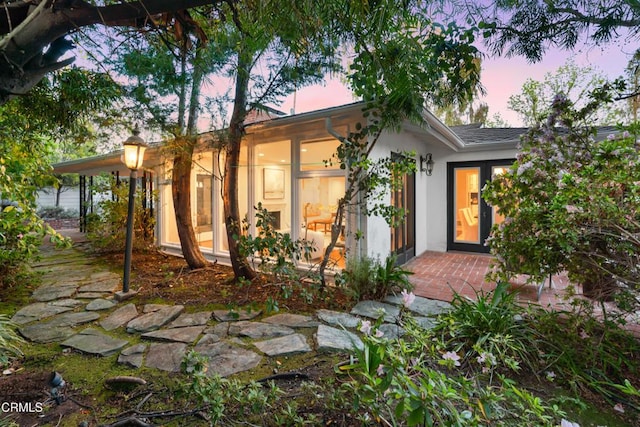 back of house at dusk with a sunroom and stucco siding