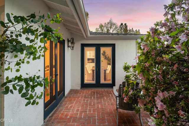 exterior entry at dusk featuring french doors and stucco siding