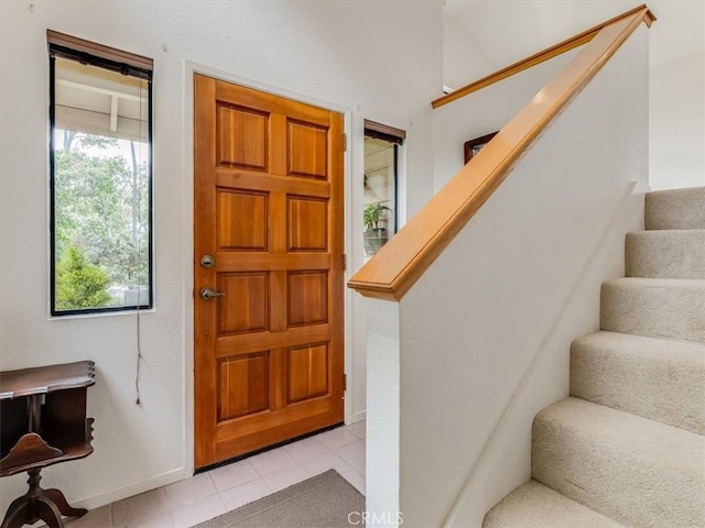 entryway featuring baseboards, light tile patterned floors, and stairway