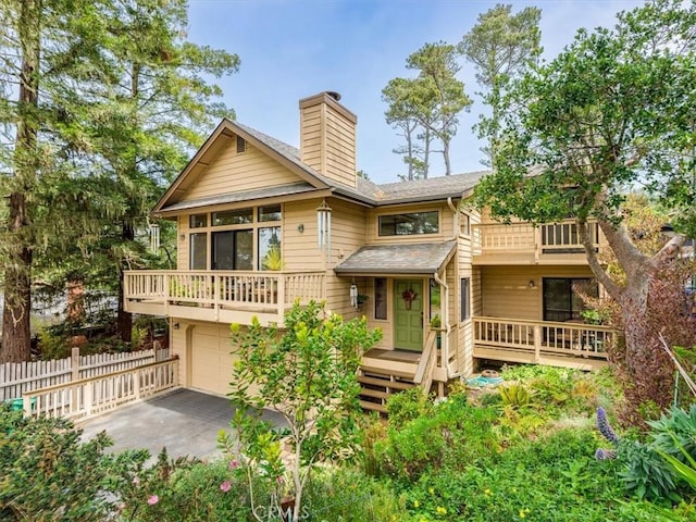 rear view of house featuring fence, an attached garage, aphalt driveway, a chimney, and a balcony