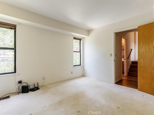 carpeted empty room featuring visible vents and stairway