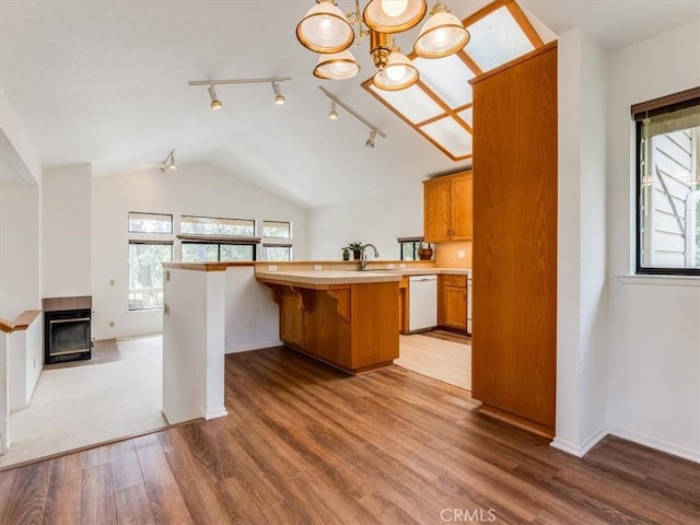 kitchen featuring white dishwasher, vaulted ceiling, wood finished floors, light countertops, and a sink