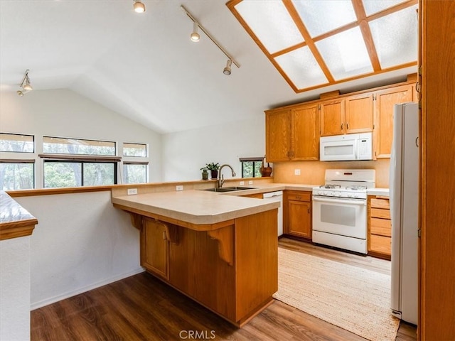 kitchen featuring a sink, a peninsula, dark wood-style floors, lofted ceiling, and white appliances