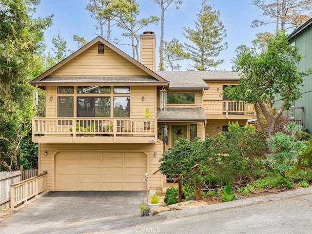 rustic home with aphalt driveway, fence, a balcony, a chimney, and an attached garage