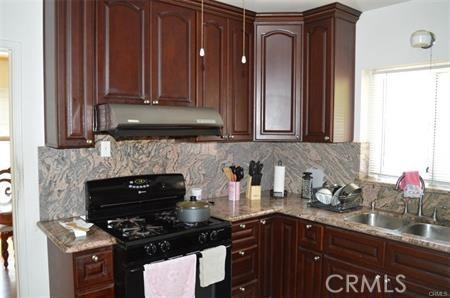 kitchen featuring a sink, decorative backsplash, black gas stove, and under cabinet range hood
