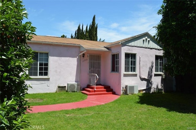 view of front of home with a front yard, central AC unit, and stucco siding