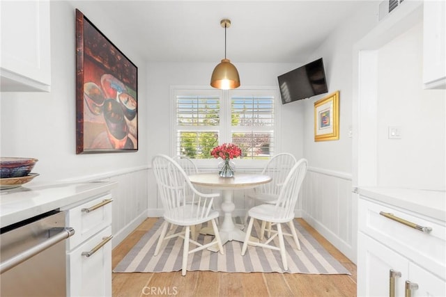 dining area featuring a decorative wall, light wood finished floors, visible vents, and a wainscoted wall