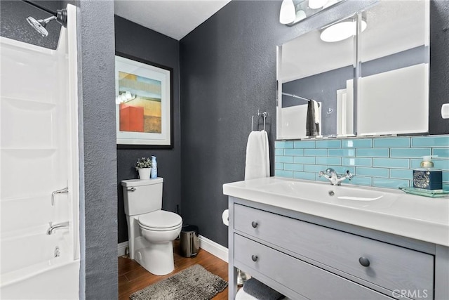 full bathroom featuring decorative backsplash, toilet, wood finished floors, washtub / shower combination, and a textured wall
